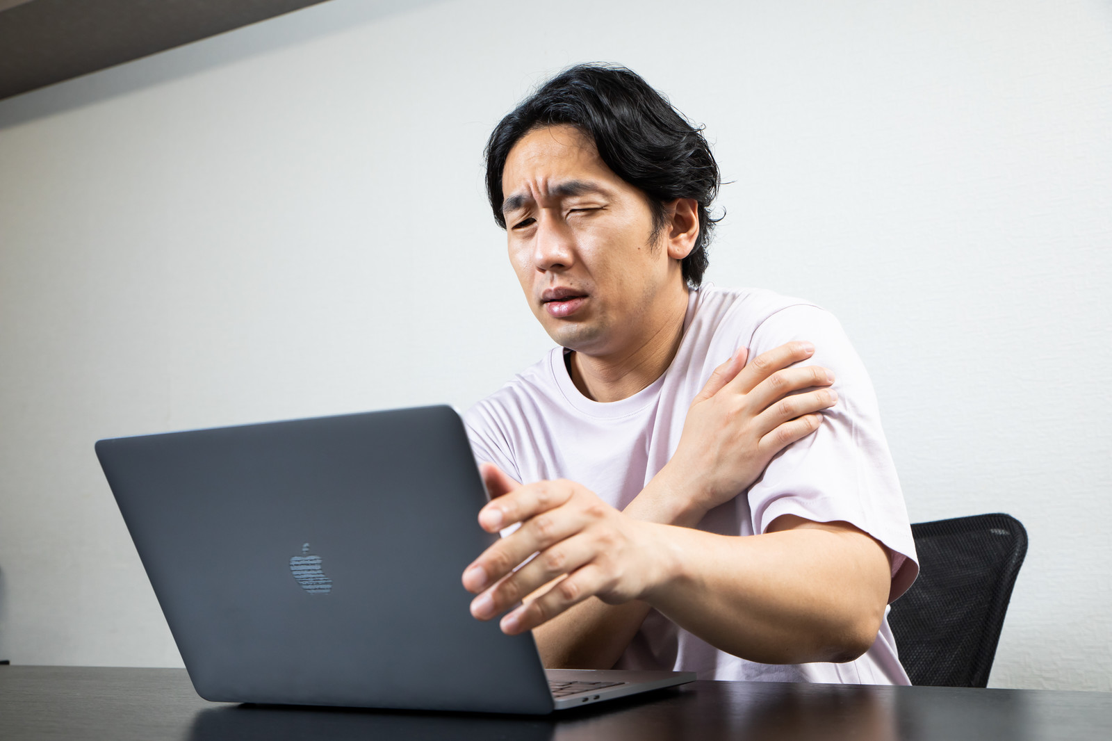 長時間のパソコンや携帯の使用によって腰や肩が痛む男性